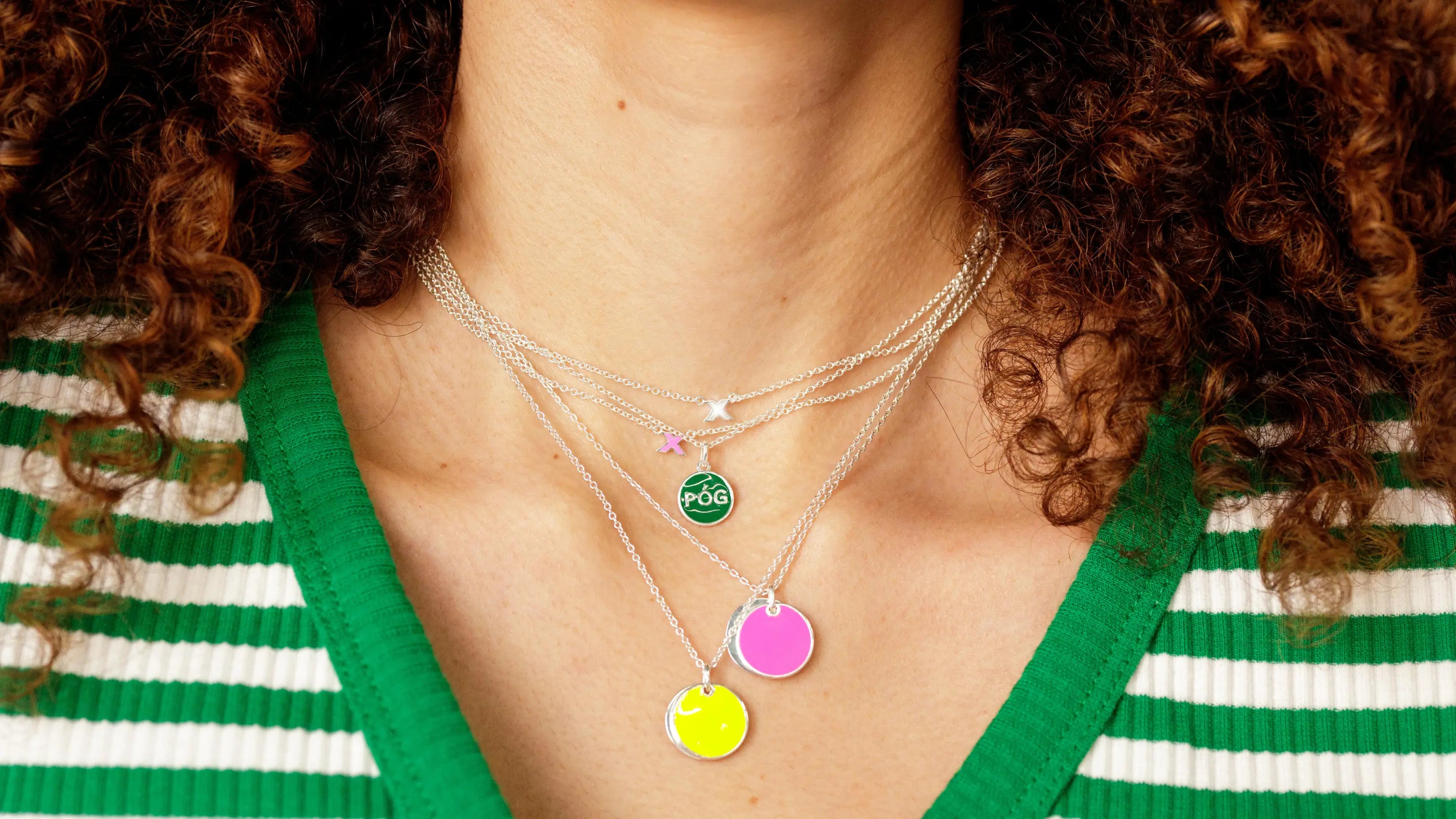 Close-up of a woman wearing PÓG's 'Locket with a Kiss' layered with other colorful enamel pendant necklaces, embodying the essence of Irish heritage and joyful connections.